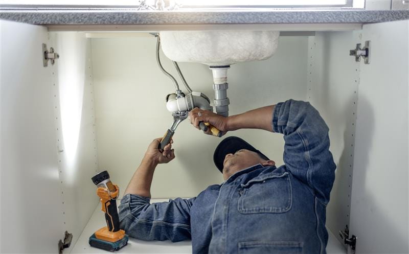 Plumber repairing pipes beneath a bathroom sink in Lynn Haven