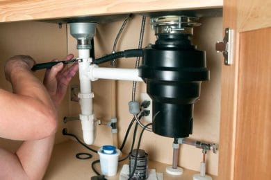 Plumber repairing a garbage disposal beneath a kitchen sink in Lynn Haven