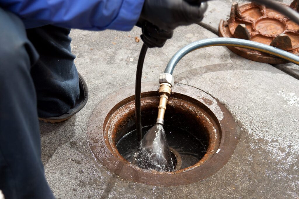 Plumber hydro jetting a sewer line through a manhole in Lynn Haven