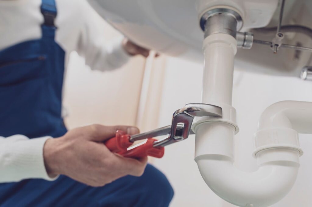 Plumber repairing a white drain pipe beneath a sink in Lynn Haven