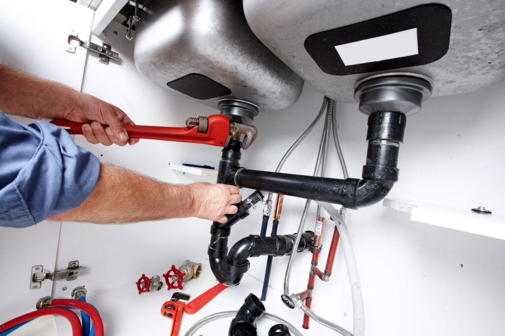 Plumber repairing drain pipes beneath a kitchen sink in Lynn Haven